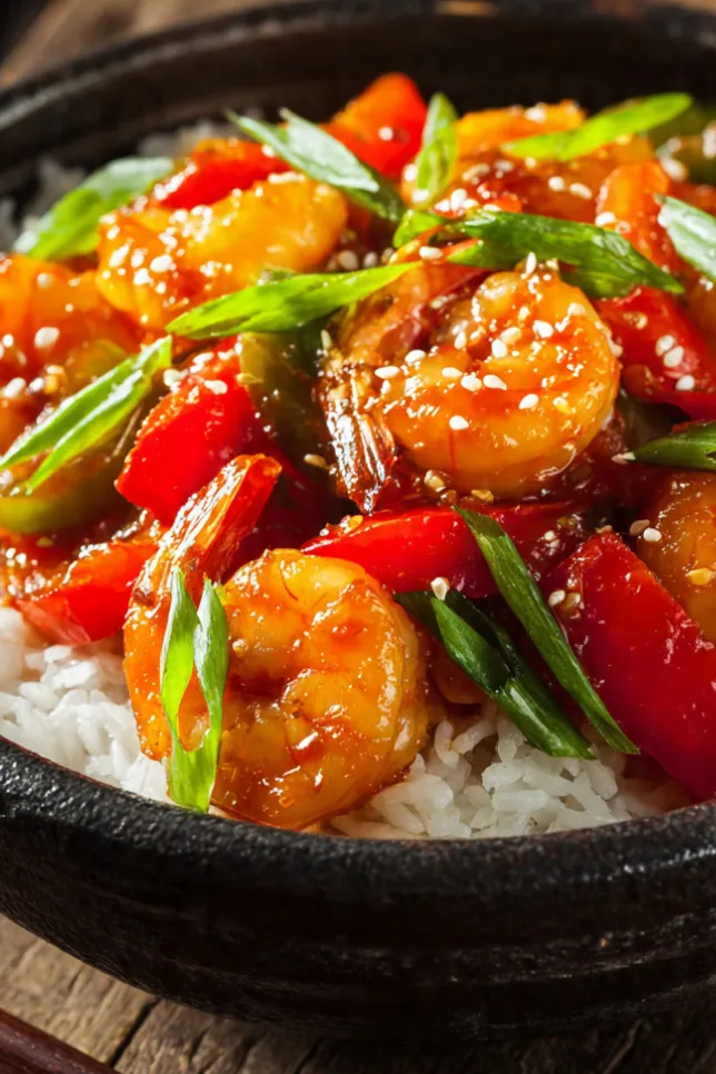 Sizzling shrimp stir-fry with red and green bell peppers in glossy sauce served over white rice in black bowl