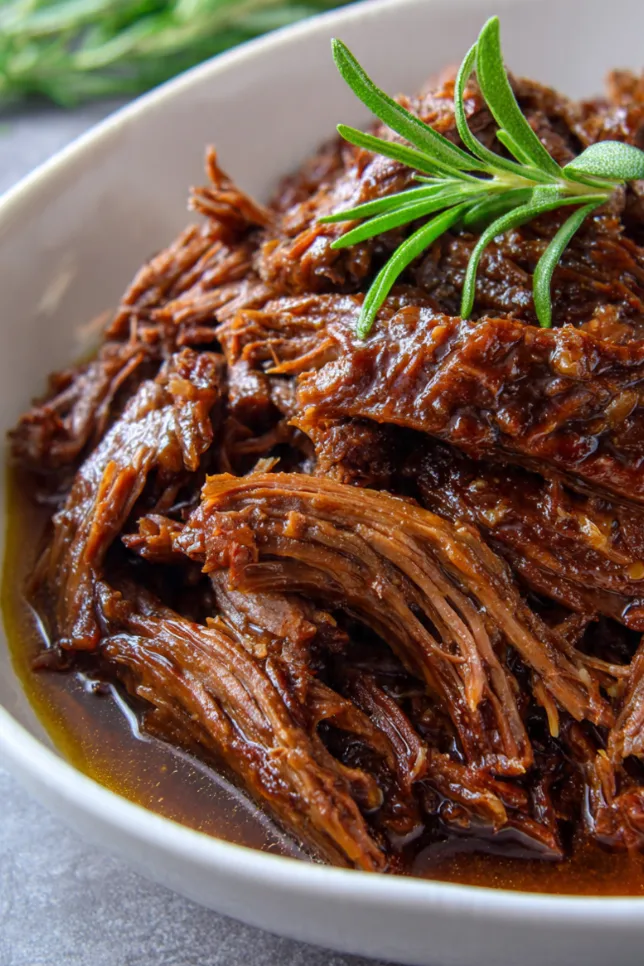Slow cooker apple cider pulled beef piled on white platter with toasted buns and coleslaw in background