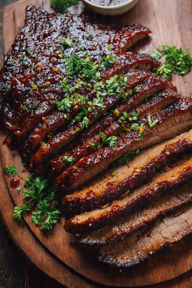 Tender sliced BBQ brisket on wooden cutting board with glossy sauce glaze and herbs