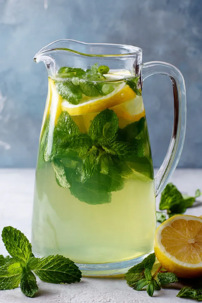 Glass pitcher of anti-inflammatory mint lemon juice with fresh mint leaves and lemon slices on a kitchen counter