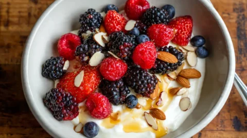 Greek yogurt protein bowl topped with fresh berries, honey drizzle, and chopped almonds in a white ceramic bowl
