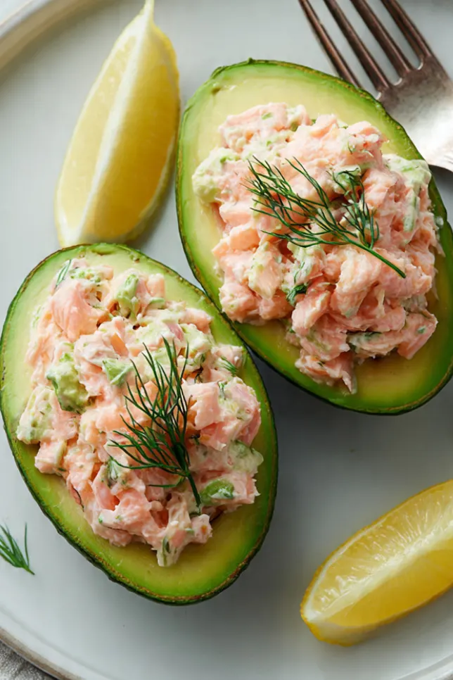 Salmon-stuffed avocado halves garnished with fresh dill on a white plate
