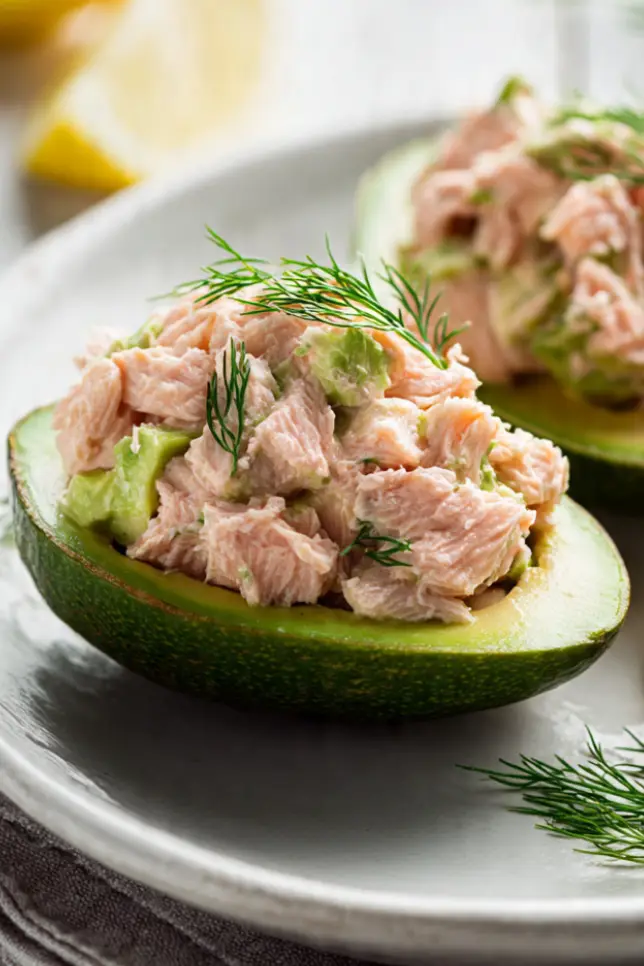 Salmon-stuffed avocado halves garnished with fresh dill on a white plate