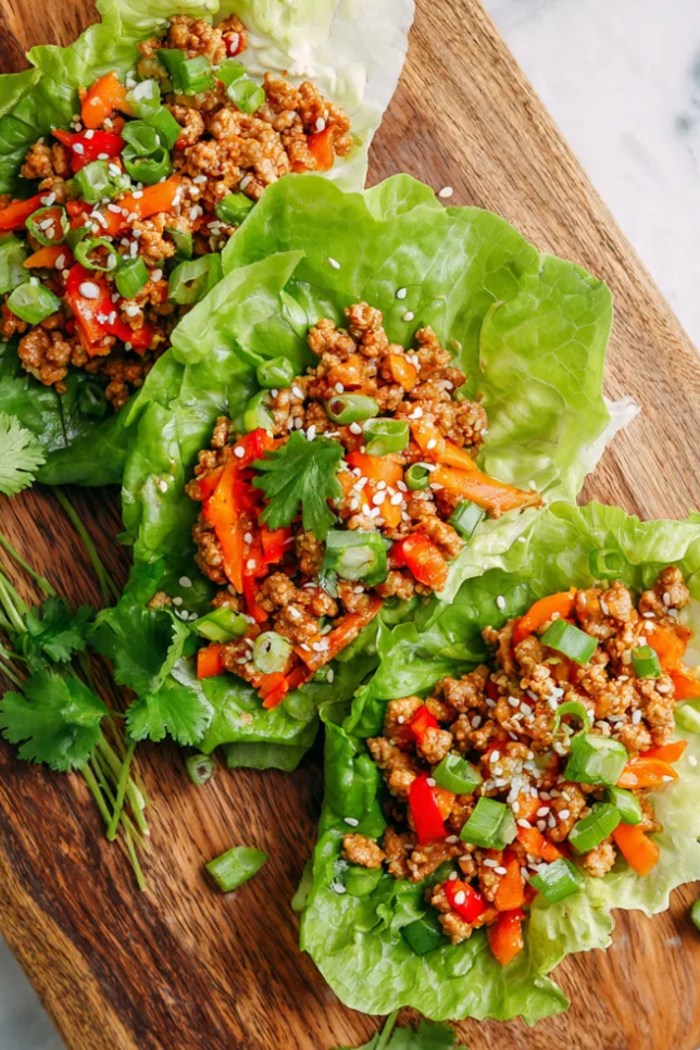 Turkey and veggie lettuce wraps with ground turkey, red bell peppers, carrots, and water chestnuts in butter lettuce cups, garnished with cilantro and sesame seeds