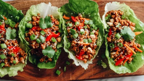 Turkey and veggie lettuce wraps with ground turkey, red bell peppers, carrots, and water chestnuts in butter lettuce cups, garnished with cilantro and sesame seeds