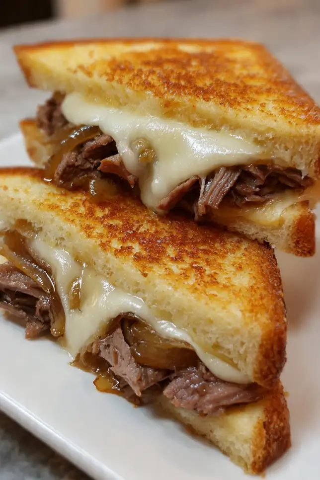 Classic beef melt sandwich with golden toasted bread, melted provolone cheese, roast beef, and caramelized onions on white plate