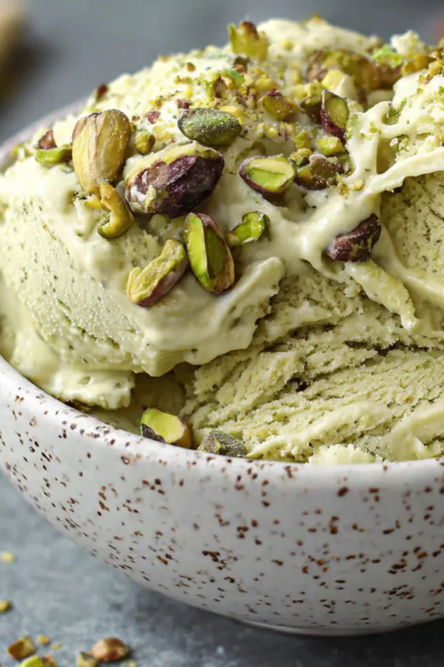 Creamy homemade pistachio protein gelato in white bowl topped with crushed pistachios on marble counter