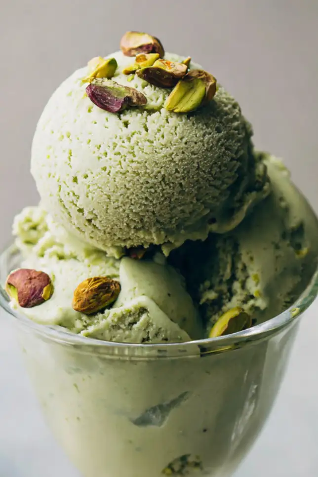 Creamy homemade pistachio protein gelato in white bowl topped with crushed pistachios on marble counter