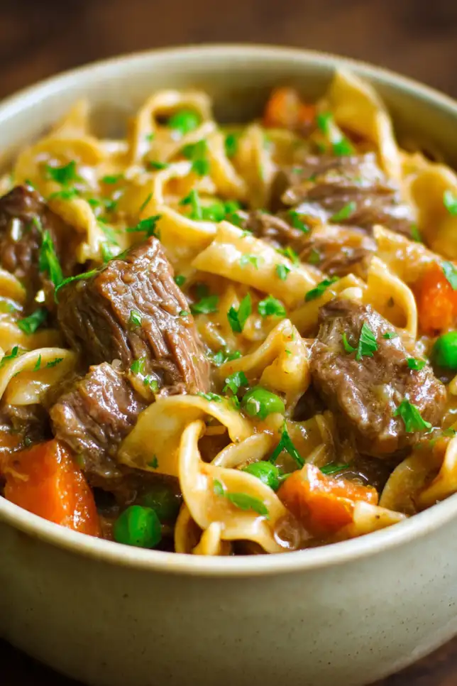 Bowl of tender crockpot beef and noodles in rich brown gravy garnished with fresh parsley on wooden table