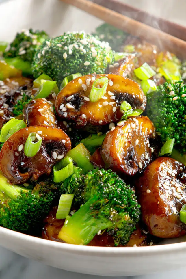 Vibrant broccoli and mushroom stir fry in white bowl with sesame seeds and green onions garnish