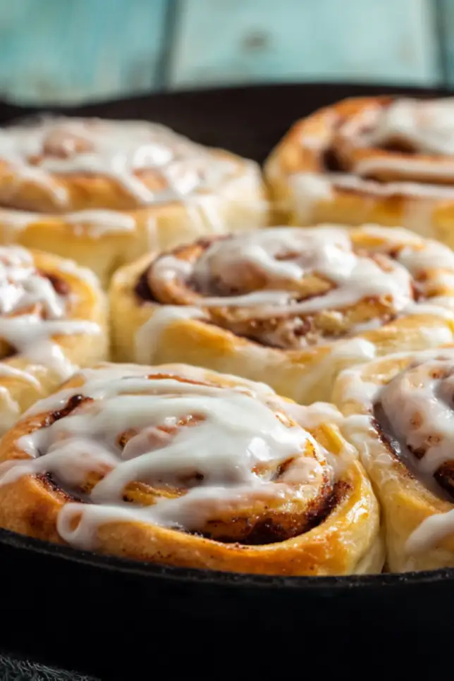 Freshly baked homemade cinnamon rolls in cast iron skillet with cream cheese frosting on rustic wooden table