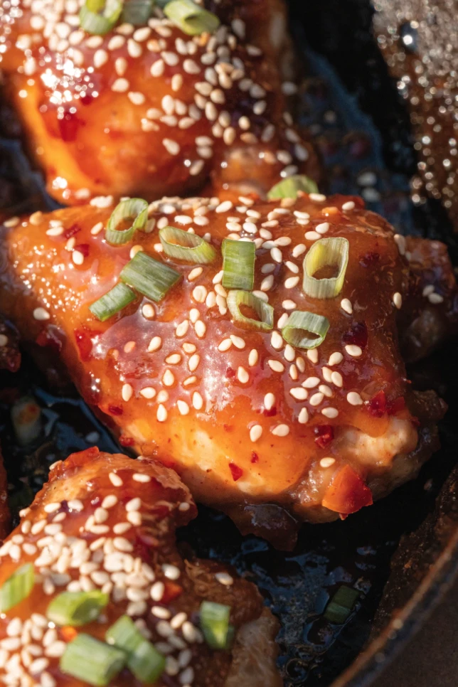 Sweet and spicy chicken thighs in a cast iron skillet with sticky honey glaze, sesame seeds, and green onions