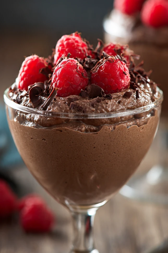 Cottage cheese chocolate mousse served in a glass jar topped with fresh raspberries and dark chocolate shavings on a wooden table