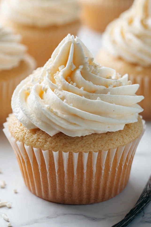 Vanilla bakery style cupcakes topped with swirled vanilla buttercream frosting on a marble countertop