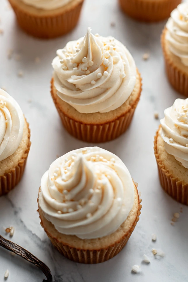 Vanilla bakery style cupcakes topped with swirled vanilla buttercream frosting on a marble countertop