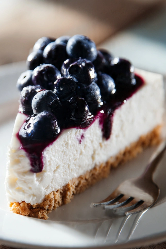 Slice of no-bake blueberry cheesecake topped with fresh blueberry compote on a white plate