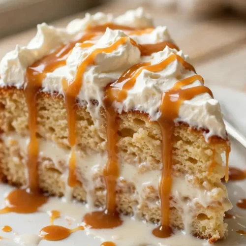 Slice of caramel tres leches cake topped with whipped cream and caramel drizzle on a white plate