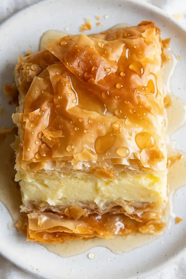 Slice of Greek galaktoboureko showing crisp phyllo layers and creamy custard center drizzled with syrup