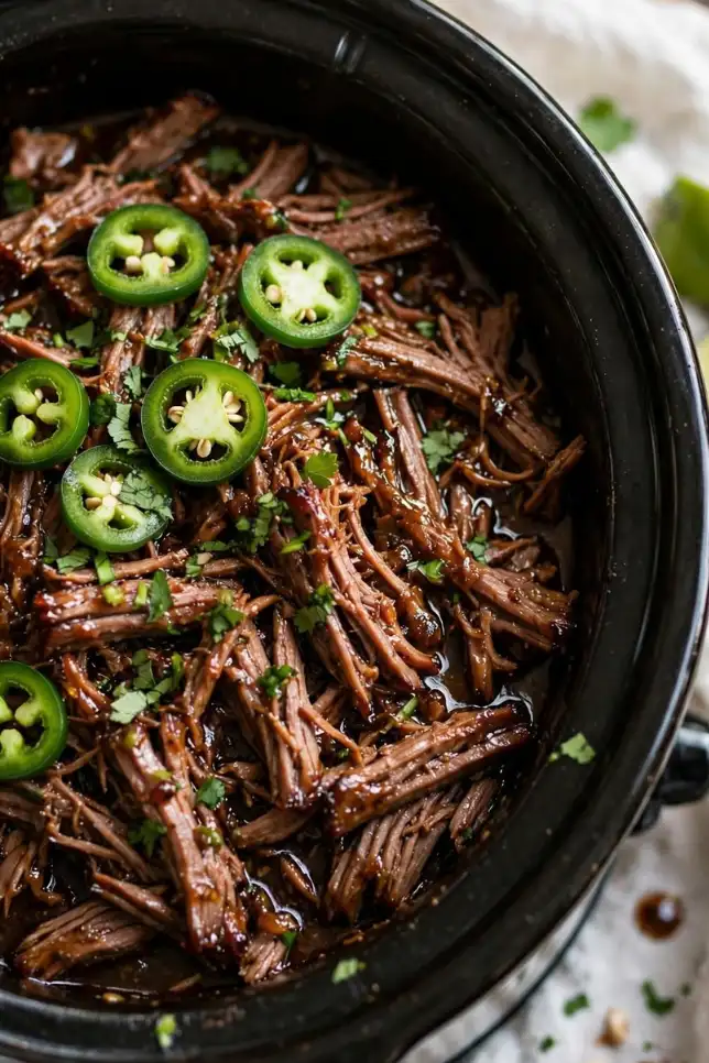 Shredded slow cooker jalapeño garlic beef topped with fresh jalapeños and cilantro