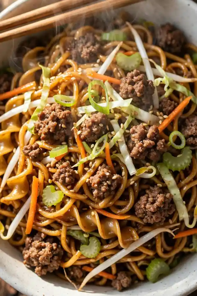 Ground beef chow mein with noodles, cabbage and carrots in a white bowl with chopsticks